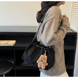 Detail of black suede bucket bag with silver chain strap and cute bear charm on shoulder