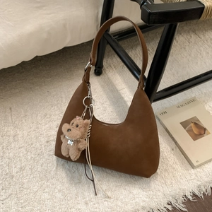 Detail of a brown suede crescent bag with a plush bear charm on a cozy carpet