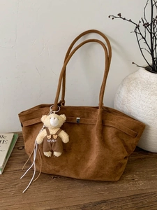 Vintage brown suede tote bag with a cute bear pendant on a rustic wooden table