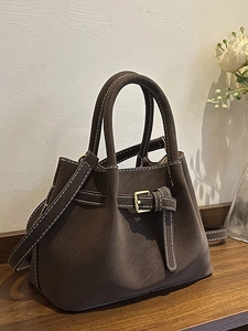 Brown suede bucket bag with contrast stitching and golden buckle on wood surface