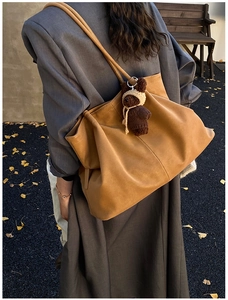 Brown leather tote bag featuring a cute teddy bear charm on autumn ginkgo leaves