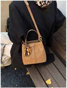 Détail d'un sac seau en cuir mat marron doté d'un accessoire pendentif en perles de bois