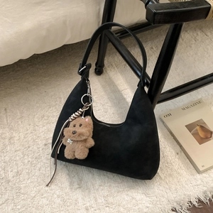 Detail of black hobo shoulder bag with a brown plush bear charm on a soft rug
