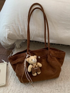 Brown suede tote bag with long strap and cute bear charm on a soft carpet setting