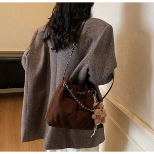 Detail of dark brown suede bucket bag with quilted stitching and plush bear charm