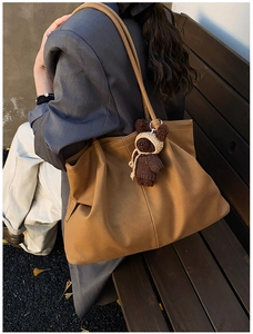 Detailed view of a brown tote bag with a knitted bear charm and vertical stitching