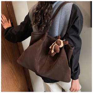 Detail view of large dark brown tote bag with cute plush bear charm on model's shoulder