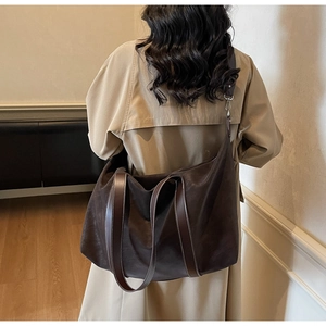 Detailed view of dark brown tote bag with contrast stitching and shoulder strap on model