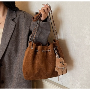 Close-up of vintage brown suede bucket bag with quilted stitching and plush bear charm