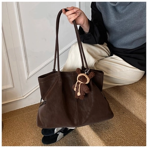 Detail of dark brown leather tote bag featuring a cute plush bear charm on the handle