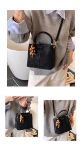 Détail du sac seau noir en daim mat avec pompon en perles de bois et anneaux métalliques