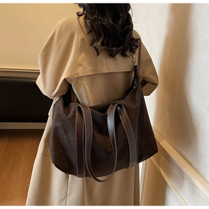 Detail of large brown tote bag with contrast stitching on leather straps worn with trench coat