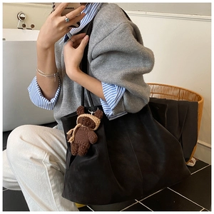 Close-up of black suede tote bag featuring pleated texture and a teddy bear pendant detail