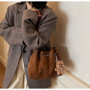 Brown suede bucket bag with quilted detail and cute bear charm worn with a blazer