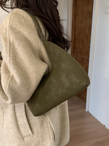 Olive green faux suede hobo bag with white stitching detail worn over a beige coat