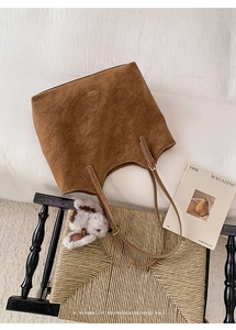 Close-up of brown suede tote bag with gold logo and plush bunny charm in a cozy setting