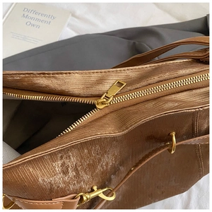 Detail of bronze metallic tote with vertical texture and gold hardware zipper and hooks