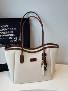 Sac fourre-tout en cuir crème avec bordure marron et breloque en perles sur fond noir