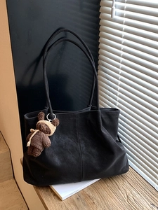 Retro black tote bag with brown bear charm on wooden table near window light