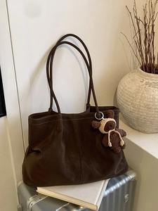 Minimalist dark brown suede tote bag with knit bear charm on a silver suitcase