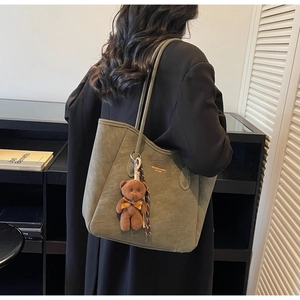Detail of olive green tote bag with matte texture and cute teddy bear charm accessory