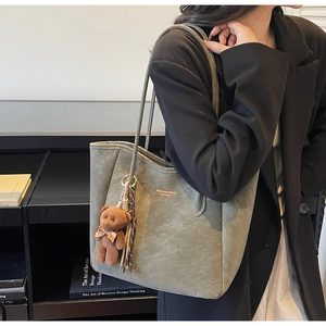 Detail of grey-green tote bag with suede texture and a plush bear charm for casual wear