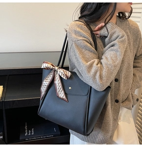 Détail d'un sac cabas en cuir grainé noir avec boucle dorée et foulard décoratif