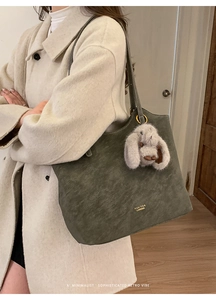 Detail of dark green suede tote bag with plush bunny charm and gold logo lettering