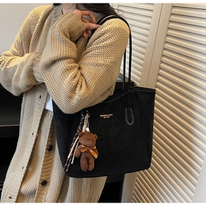Close-up of black suede tote bag with golden lettering and a cute bear charm detail