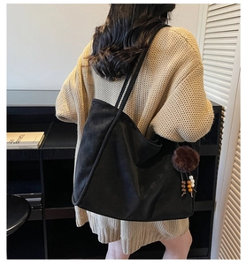 Dettaglio di una grande borsa tote in pelle scamosciata nera con ciondolo a pompon marrone