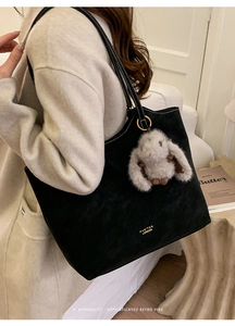 Detail of black matte tote bag with gold branding, rabbit charm and white stitching