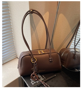Macro detail of dark brown pebble leather bowling bag with gold zipper and pretzel charm