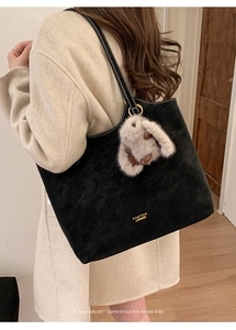 Retro black tote bag with matte texture and cute plush bunny charm on a beige coat model
