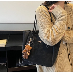 Detail of black large tote bag with contrast stitching and a cute bear plush charm