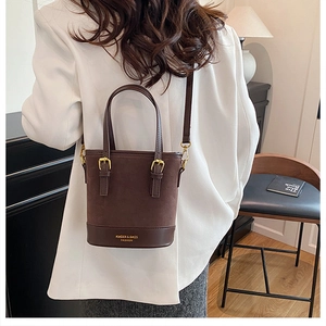 Detail of a dark brown suede bucket bag featuring contrast stitching and gold buckle