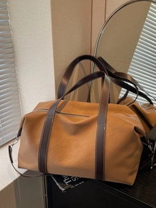 Large vintage camel leather travel tote bag with brown handles on a minimalist cabinet