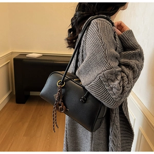 Model wearing a black litchi leather boston bag with gold zipper and woven charm detail