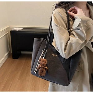 Detail of dark brown tote bag with plush bear charm and metallic logo worn on model