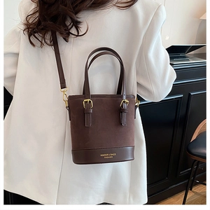 Detail of a brown bucket bag showing suede and faux leather texture with gold metal buckles