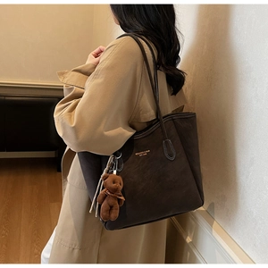 Detail of large brown tote bag featuring embossed logo and cute plush bear charm accessory