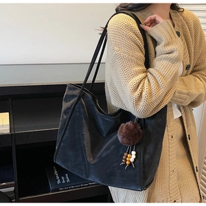 Dettaglio borsa tote in ecopelle nera con ciondolo a pompon marrone e decoro di perle