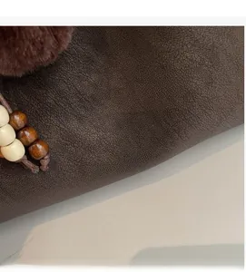 Close-up of brown textured leather tote bag with gold logo and plush charm detail