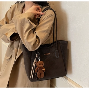 Detail of vintage brown tote bag with plush bear charm and brand logo print
