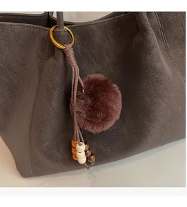 Close-up of brown litchi pattern leather tote bag with plush ball and wooden bead charm