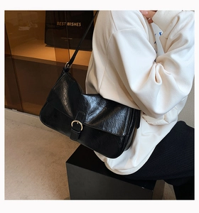 Detail view of the black soft leather shoulder bag with golden buckle on a white sweater