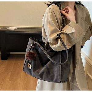 Dettaglio della borsa shopper grigio scuro con ciondolo in peluche su trench casual