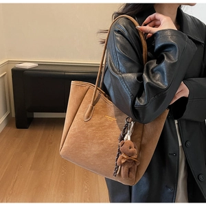 Detail of a brown suede tote bag with a cute plush bear charm and metallic logo accents
