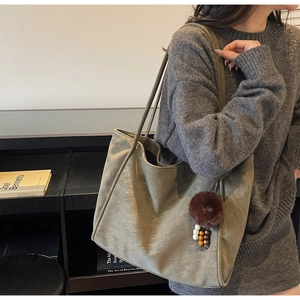 Borsa tote verde grigiastra con ciondolo di peluche portata a spalla da modella