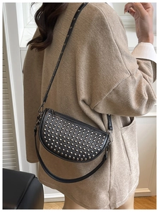 Detail of black crescent crossbody bag featuring silver rivets and dual strap design