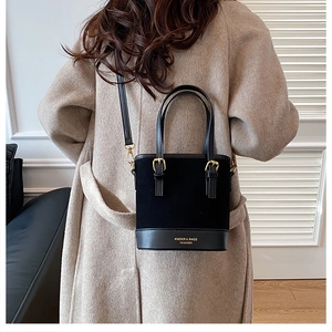 Detail view of a black bucket bag with a mix of suede and smooth leather on a model